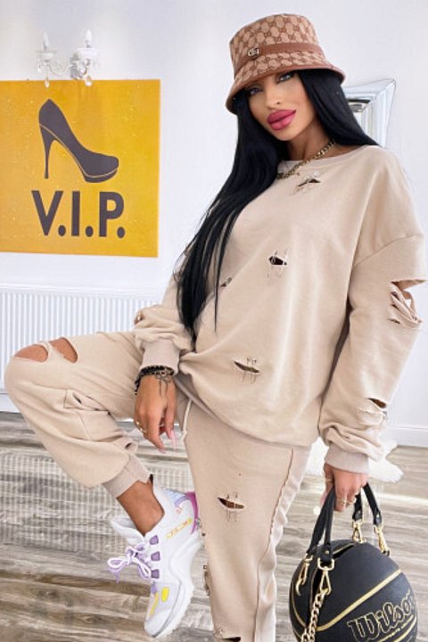 2-piece beige set, consisting of oversized blouse and trousers with elastic at the ankles. Model with cuts across the entire surface.